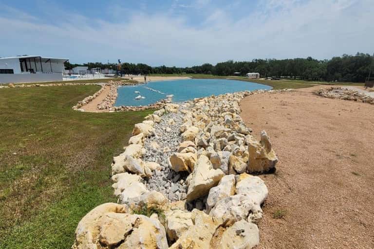 Turquoise lagoon with rock border, manicured lawn, and white building structures in background