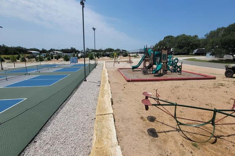 Pickleball courts with blue and green playing surfaces next to playground equipment and water features