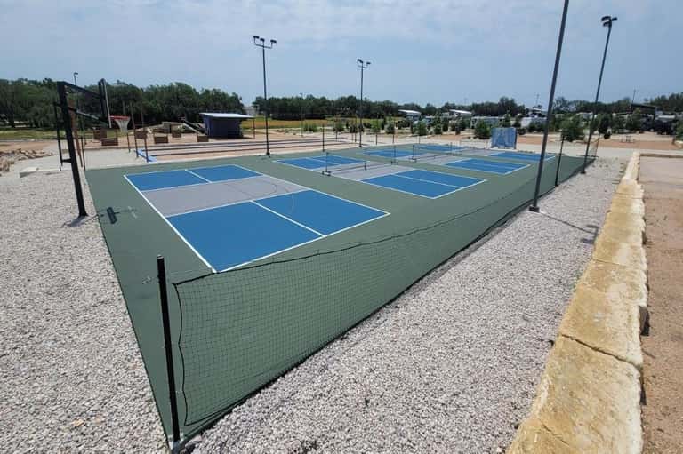 Multiple pickleball courts with blue and green surfaces, fencing, and tall light poles
