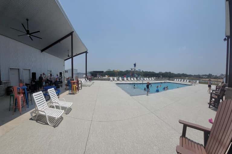 Resort pool area with covered pavilion seating, loungers, and people swimming in afternoon light