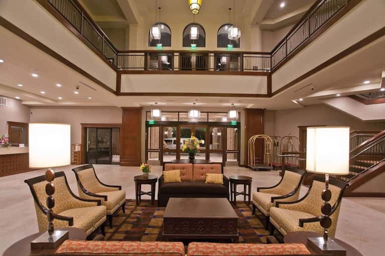Elegant hotel lobby with high ceilings, two-story balcony, gold-patterned upholstered chairs, and central seating arrangement