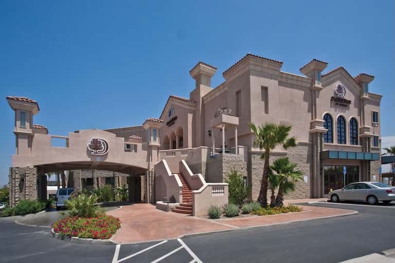 Mediterranean-style resort exterior with pale stone facade, arched windows, palm trees, and red brick courtyard