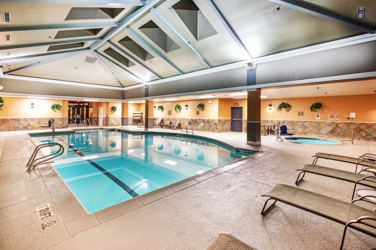 Indoor hotel pool with skylight ceiling, orange walls, tile accents, lounge chairs, and spa area