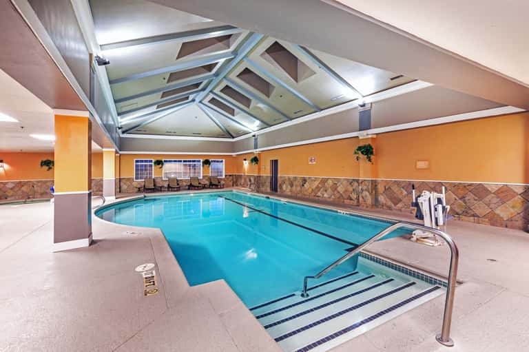 Indoor pool facility with vaulted skylight ceiling, orange accent walls, tile features, and lounge seating