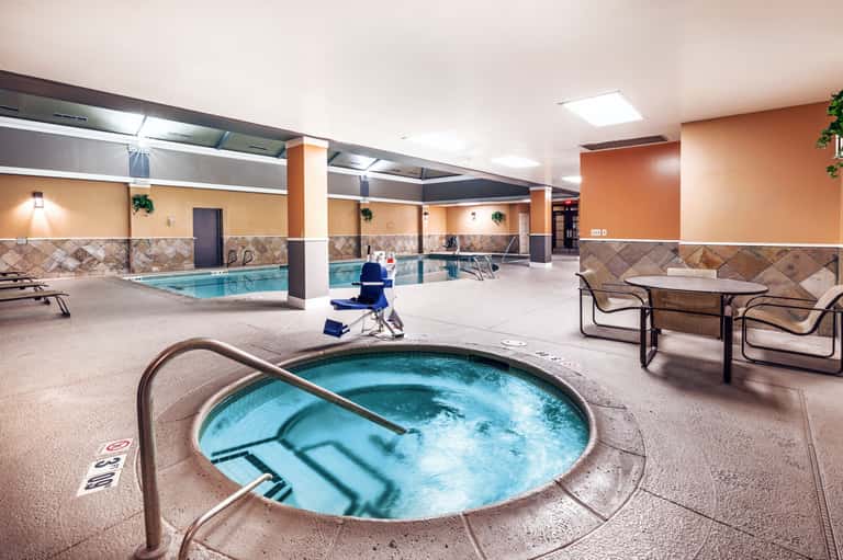 Indoor pool complex with hot tub in foreground, orange and tan walls, multiple seating areas, and columns