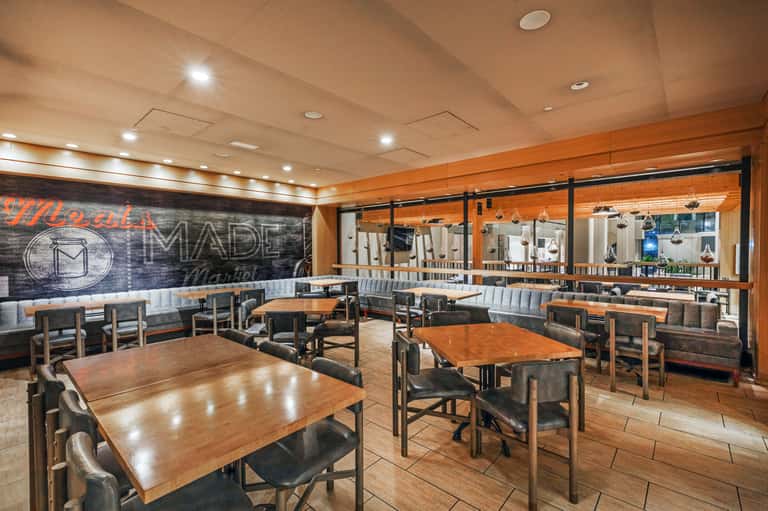 Hotel restaurant interior with wooden tables, booth seating, decorative wall signage, and large mirror panels