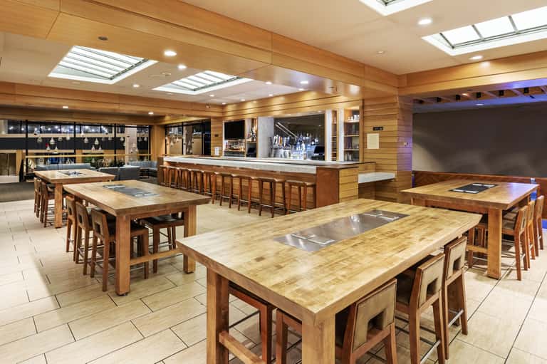Modern culinary kitchen with wooden tables, chef stations, bar seating, and skylight ceiling