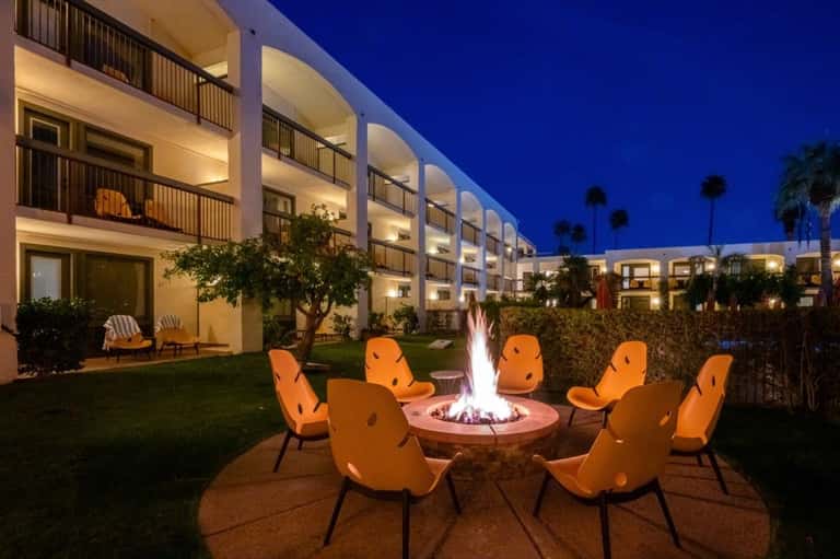 Evening fire pit gathering area with orange chairs surrounded by modern white hotel buildings and palm trees