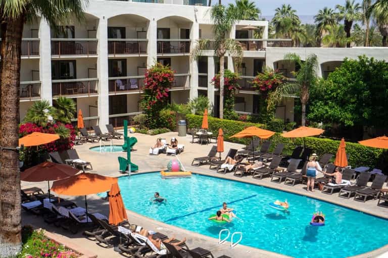 Resort pool with turquoise water, orange umbrellas, lounge chairs, and white Mediterranean-style architecture