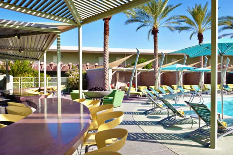Modern pool area with pergolas, colorful lounge chairs, umbrellas, and palm trees under clear sky