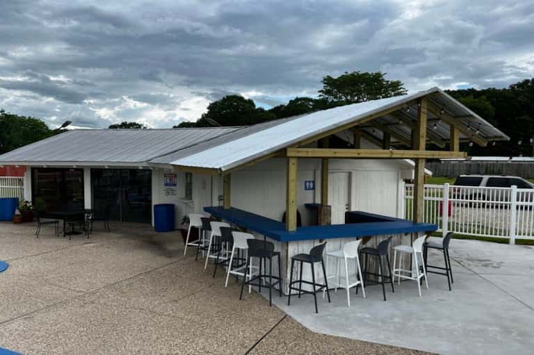 Outdoor bar and lounge area with blue countertop, modern shelter structure, and parking area