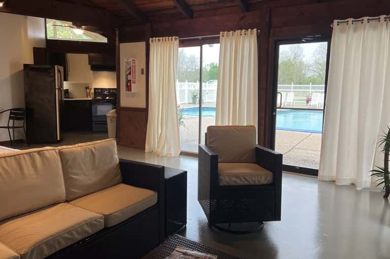 Resort lounge interior with brown furniture, full kitchen, glass doors overlooking pool and patio