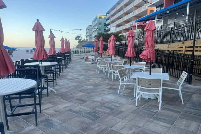 Beachfront terrace with pink umbrellas, white furniture, string lights, and multi-story hotel building