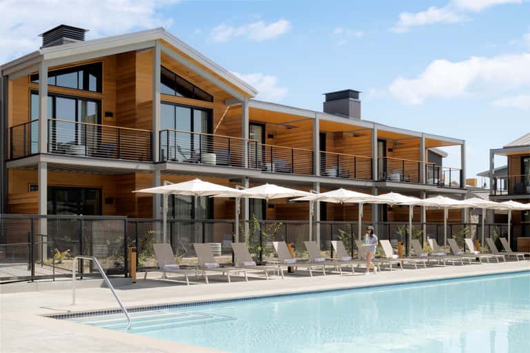 Contemporary resort with wooden facade, white umbrellas, lounge seating, and blue pool