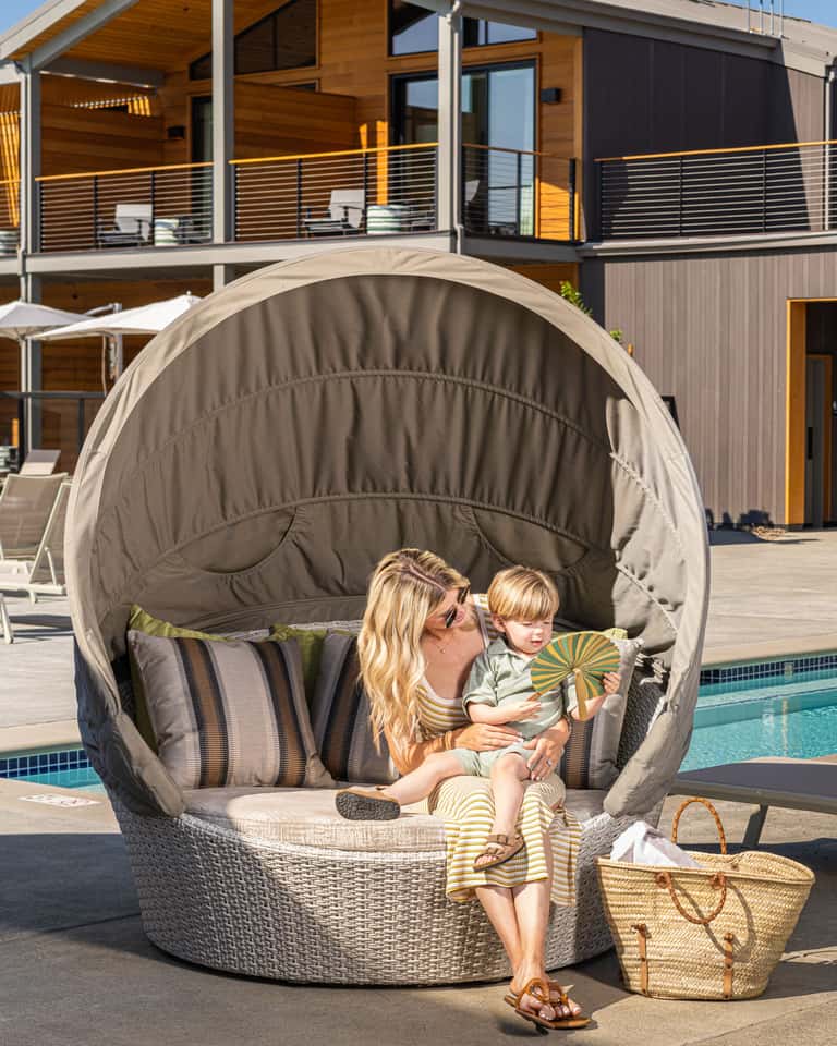 Woman and toddler in beige dome pod chair by resort pool overlooking water