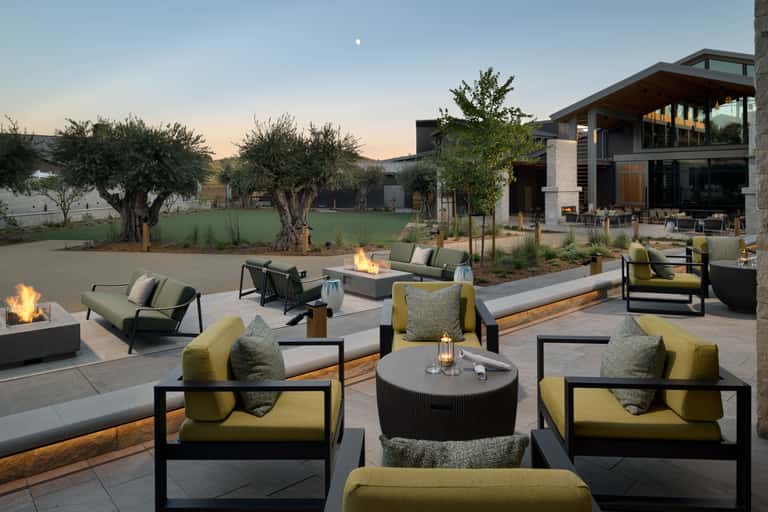 Upscale outdoor lounge at dusk with fire pits, seating groups, and modern building architecture