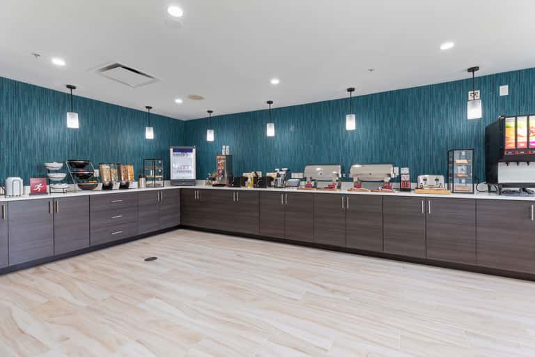 Modern coffee bar with teal accent wall, espresso machines, pastry display, and beverage service counter