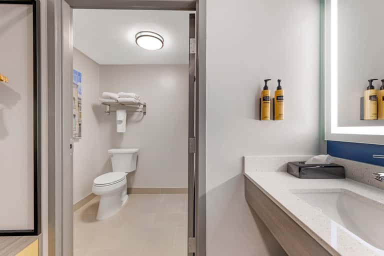 Clean bathroom vanity with sink, mirror, toiletries, and adjacent toilet in hotel room