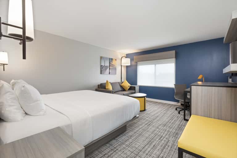 Spacious hotel room featuring queen bed, blue wall, yellow chair, and seating area