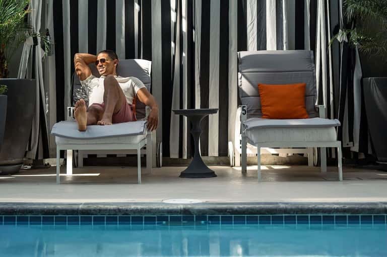 Guest relaxing on poolside lounge chair with striped privacy screens and pool view