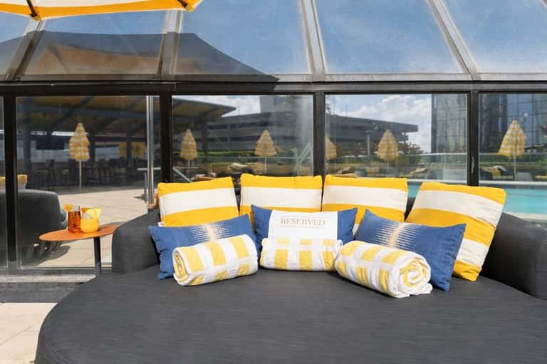 Reserved circular sunbed with yellow-white striped cushions and pillows overlooking pool area
