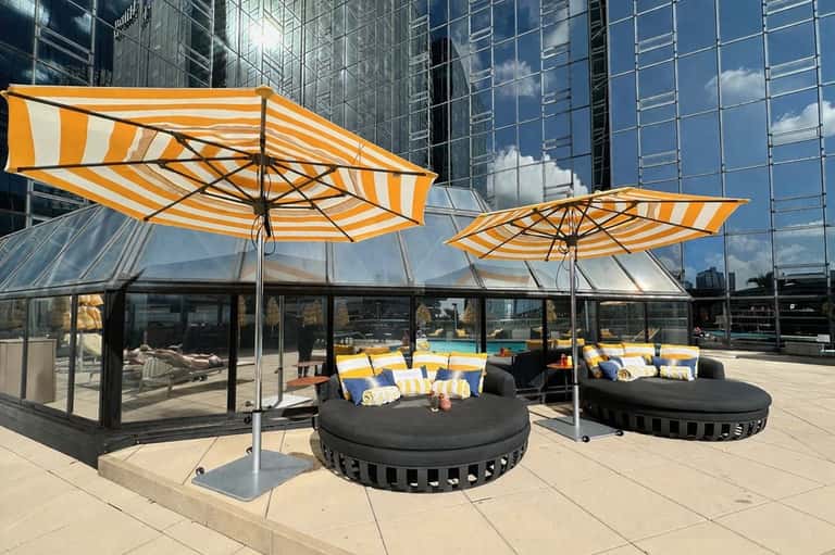 Rooftop terrace with round sunbeds, yellow umbrellas, glass pavilion, and city skyline views