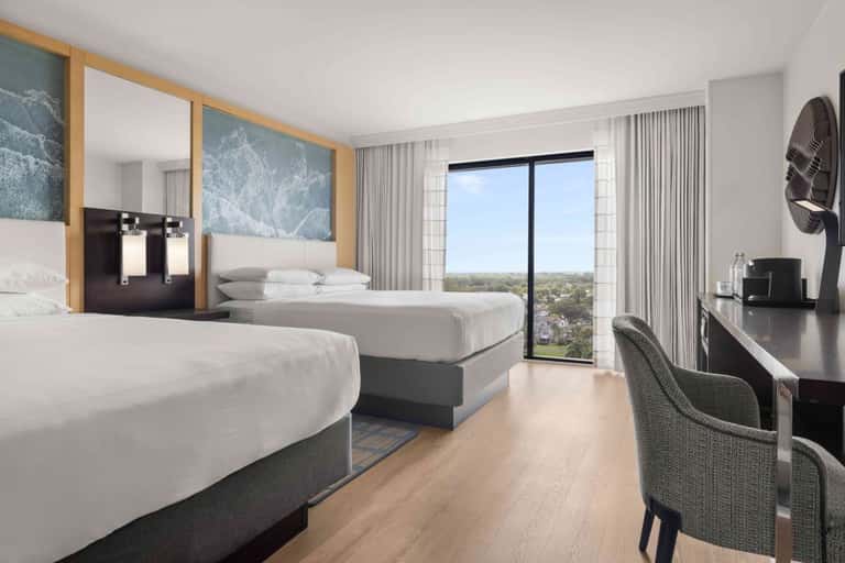 Modern hotel room with two queen beds, ocean view balcony, wooden accents, and contemporary furnishings