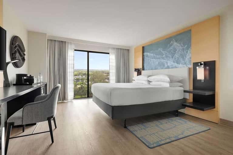 Modern hotel bedroom with king bed, work desk, balcony with panoramic views, and contemporary decor