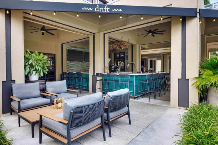 Outdoor patio lounge with turquoise bar seating, gray upholstered furniture, and tropical plants