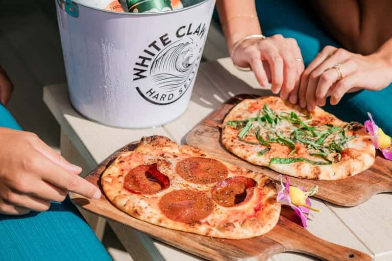 White Claw hard seltzer bucket with gourmet pizzas on wooden serving boards