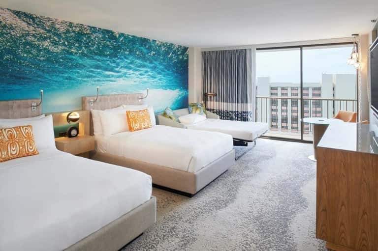 Beachfront hotel room with two beds, ocean mural headboard, and ocean view balcony