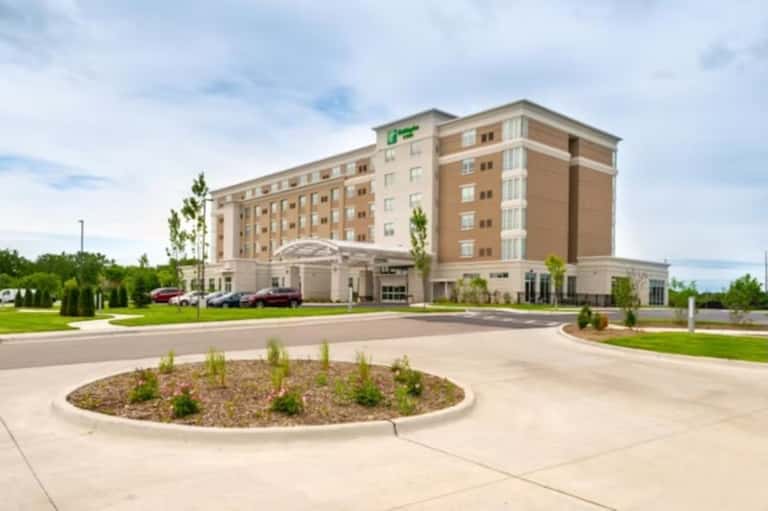 Modern hotel exterior showing multi-story brick building with green signage, entrance, and landscaped grounds