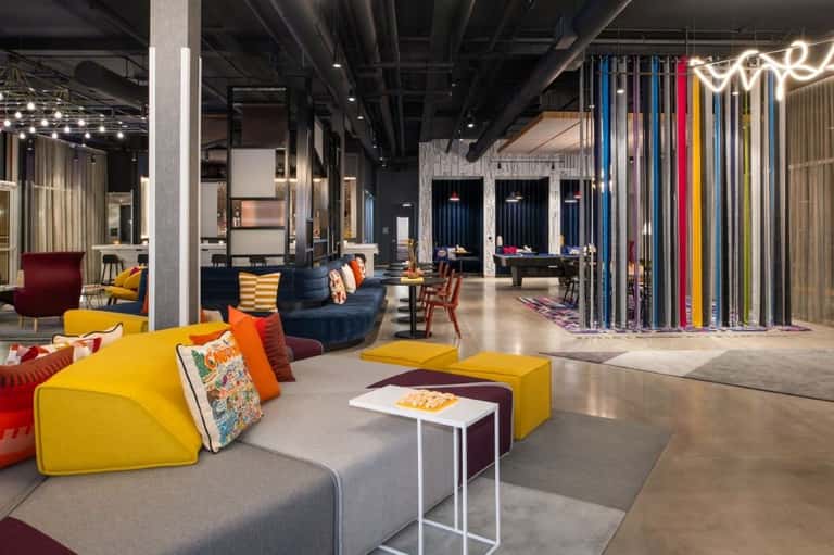 Modern hotel lounge with yellow modular seating, colorful accent pillows, dark blue furniture, and vibrant neon signage
