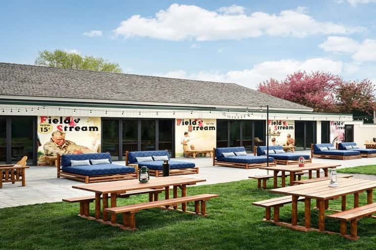 Field & Stream outdoor patio with wooden picnic tables, blue cushioned lounge chairs, and vintage signage