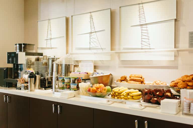 Hotel breakfast buffet with coffee station, fresh fruits, pastries, and baked goods on white counter
