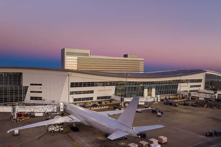 Commercial aircraft parked at airport terminal gate with modern hotel building illuminated at dusk