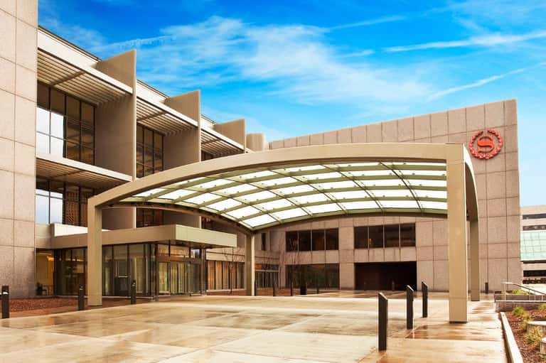 Modern hotel entrance with curved glass canopy and beige stone facade under blue sky