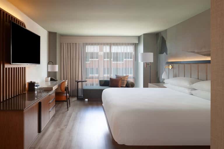 Modern hotel room with two queen beds, work desk, flat-screen TV, and floor-to-ceiling windows with city views