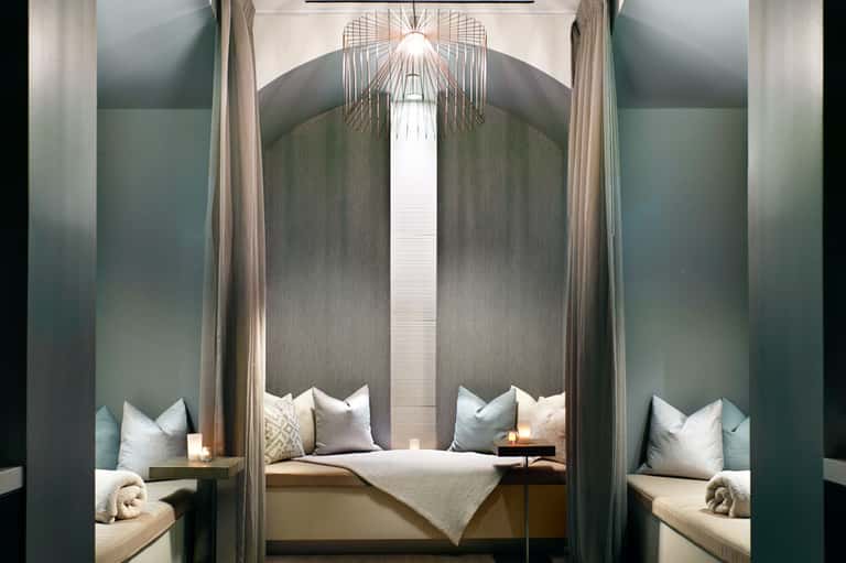 Luxurious bedroom alcove with grey upholstered walls, white pillows, and modern geometric ceiling fixture