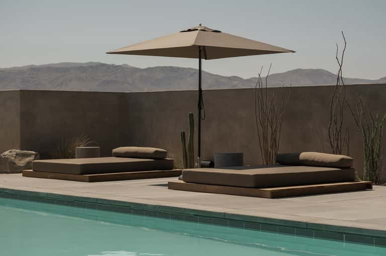 Poolside lounge with low platform seating, umbrella, desert landscape view, and architectural landscaping