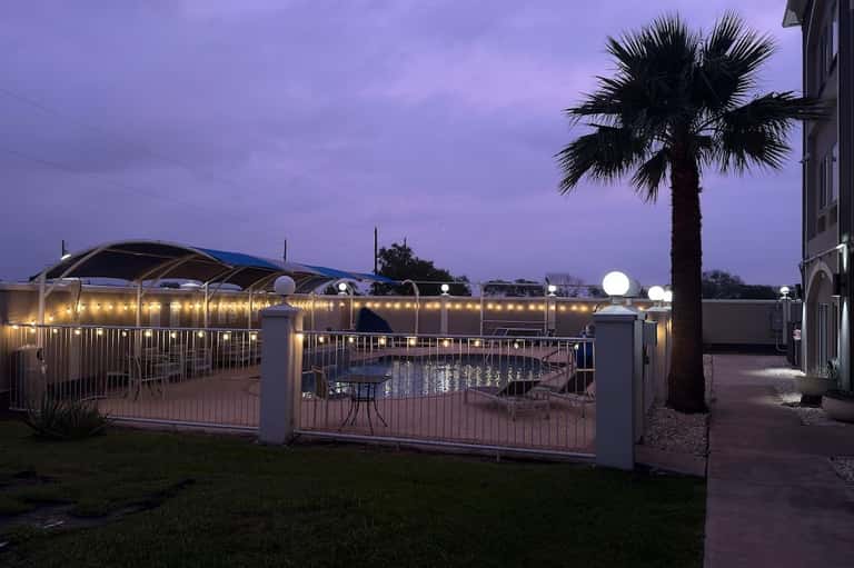 Gated pool area with palm tree, cabanas, and ambient lighting at twilight