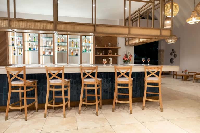 Upscale resort bar with wooden bar stools, illuminated liquor display, and pendant lighting