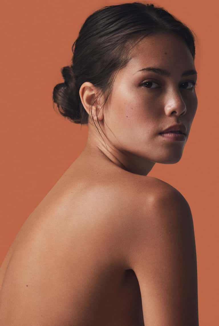 Portrait of woman with bare shoulders against warm orange background