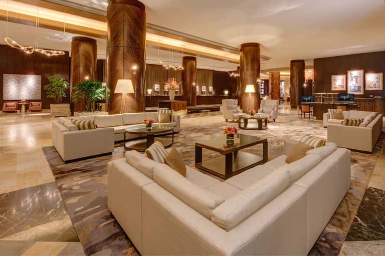 Luxury hotel lobby featuring marble floors, wooden columns, cream seating areas, and contemporary artwork