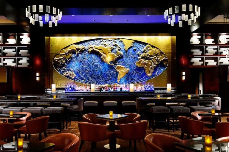 Upscale hotel bar lounge with artistic world map backdrop, modern chandelier, leather seating, and ambient lighting