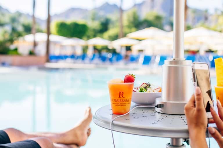 Orange cocktail with strawberry garnish on umbrella table overlooking resort pool