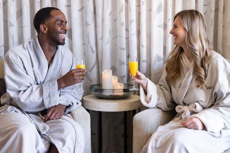Couple in white robes toasting with champagne by candlelight in elegant room setting