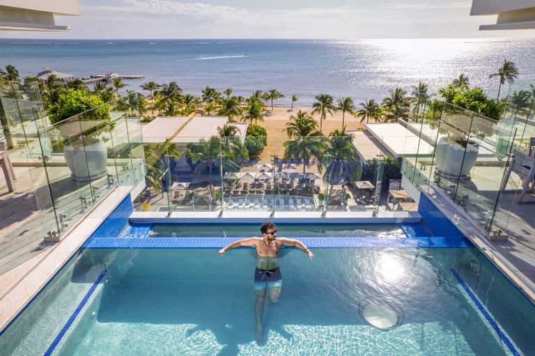 Man swimming in rooftop infinity pool with ocean and palm trees in background
