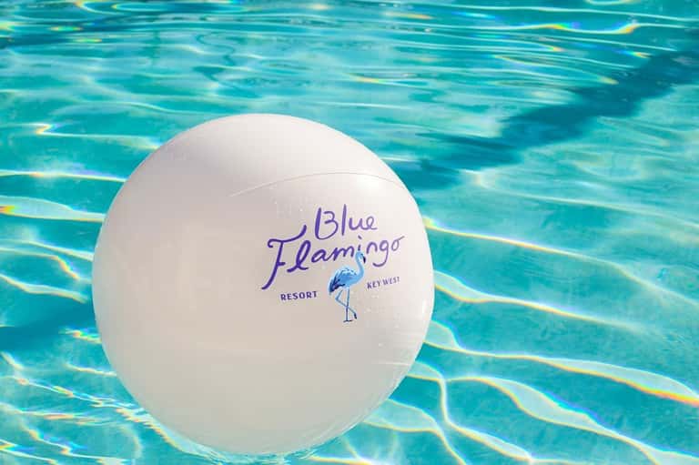 White beach ball floating in turquoise pool water with Blue Flamingo Resort branding