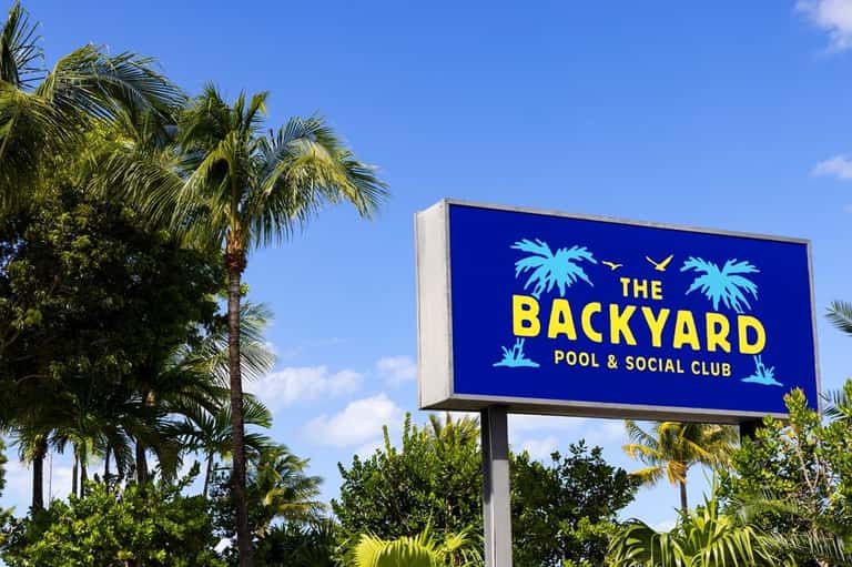 The Backyard Pool & Social Club sign with palm trees against blue sky